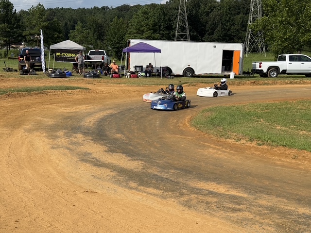 Karts running side by side down the clay with the haulers in the background