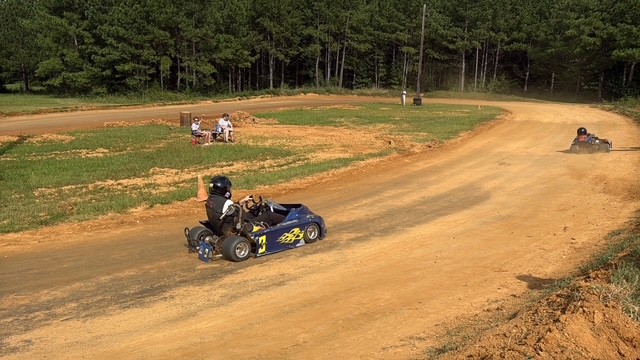 Ronnie's blue 3 kart running the clay with the pines behind the track