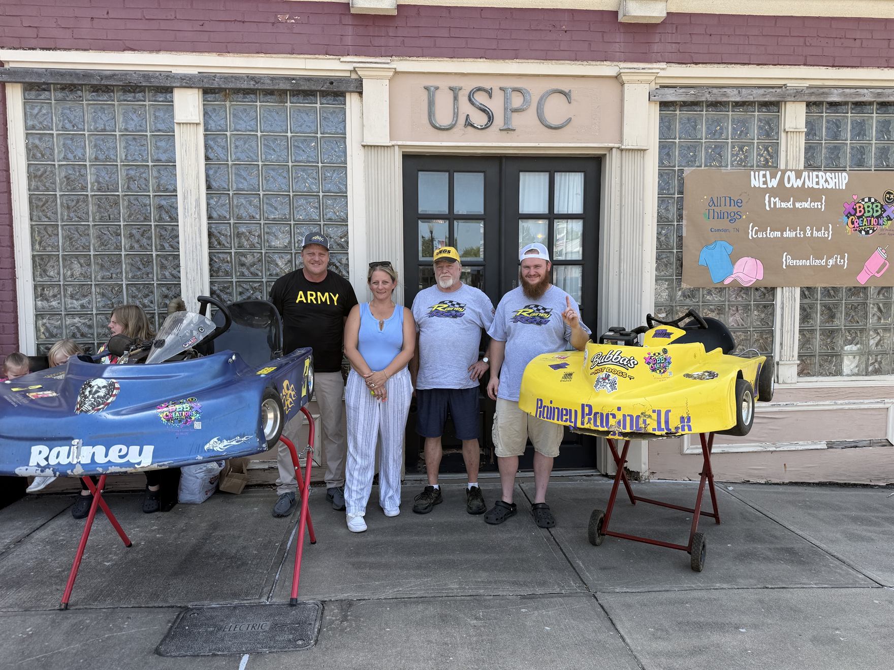 Ronnie Rainey, shop and BBB Creations owner Brandi Bath, Ronnie Rainey Sr. and Travis Rainey standing with both karts outside the shop on the Camden Court Square