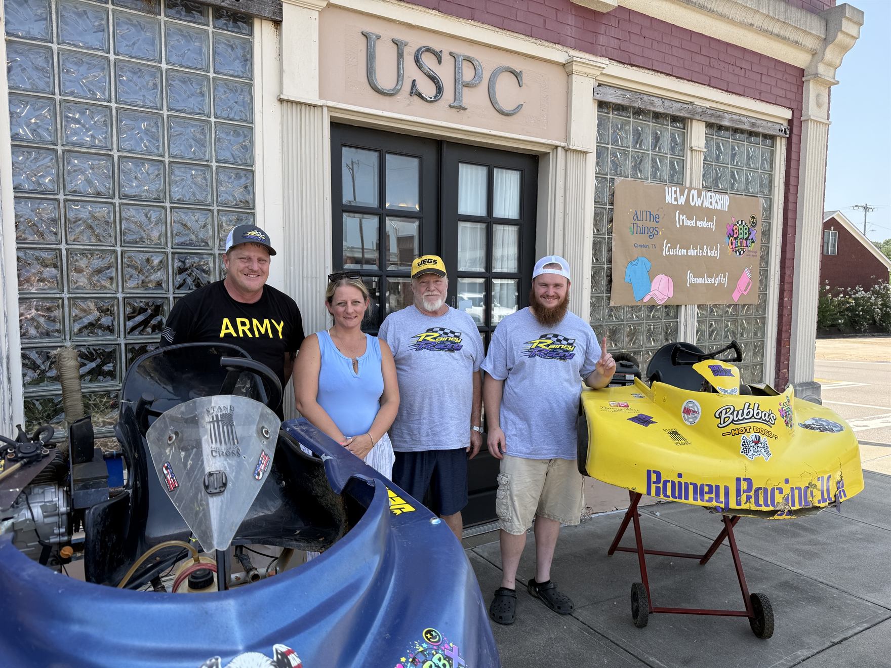 Ronnie Rainey, Brandi Bath, Ronnie Rainey Sr. and Travis Rainey with both karts in front of the shop's New Ownership sign