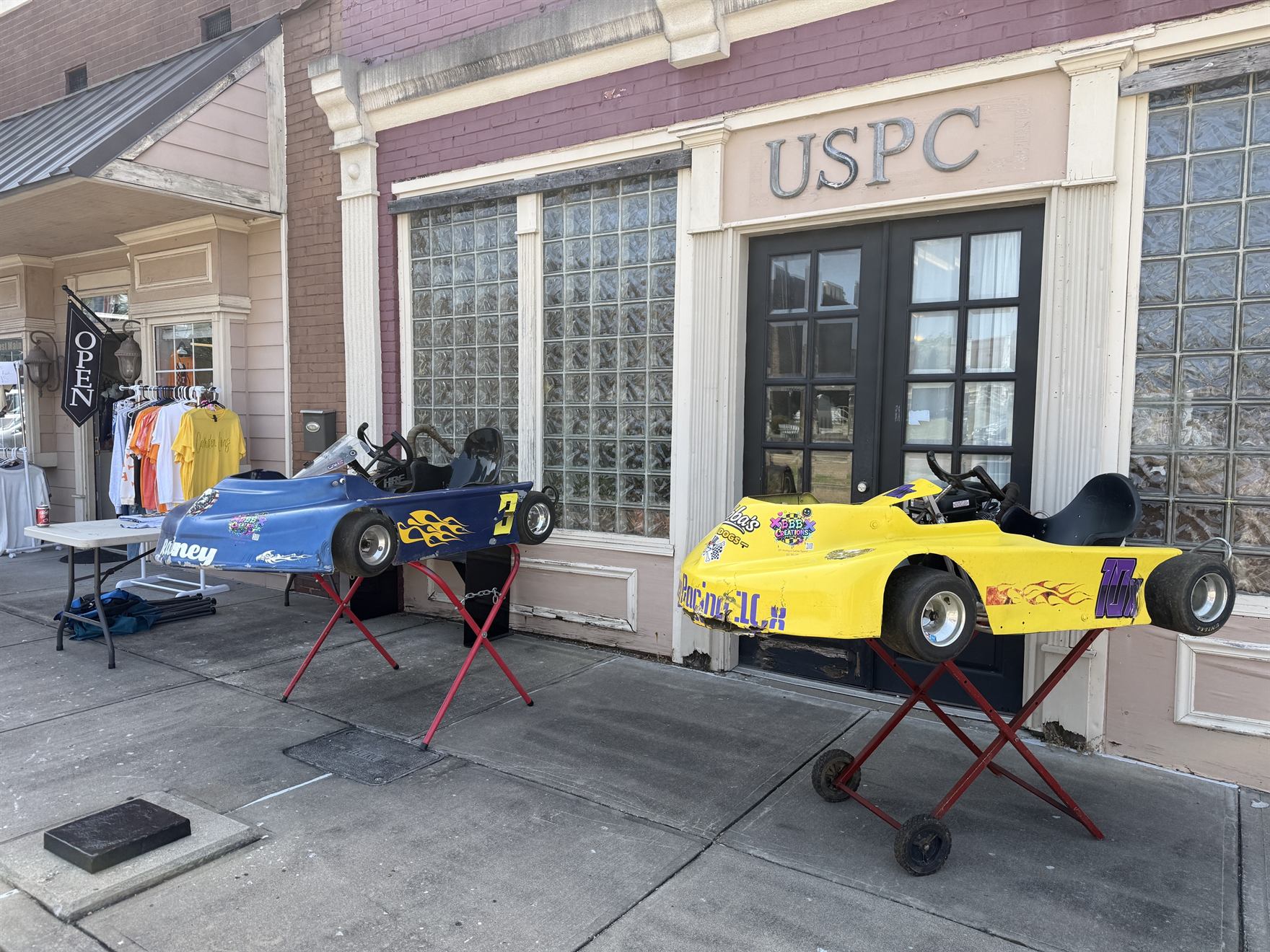 The blue 3 and yellow 10X karts up on their stands on the sidewalk