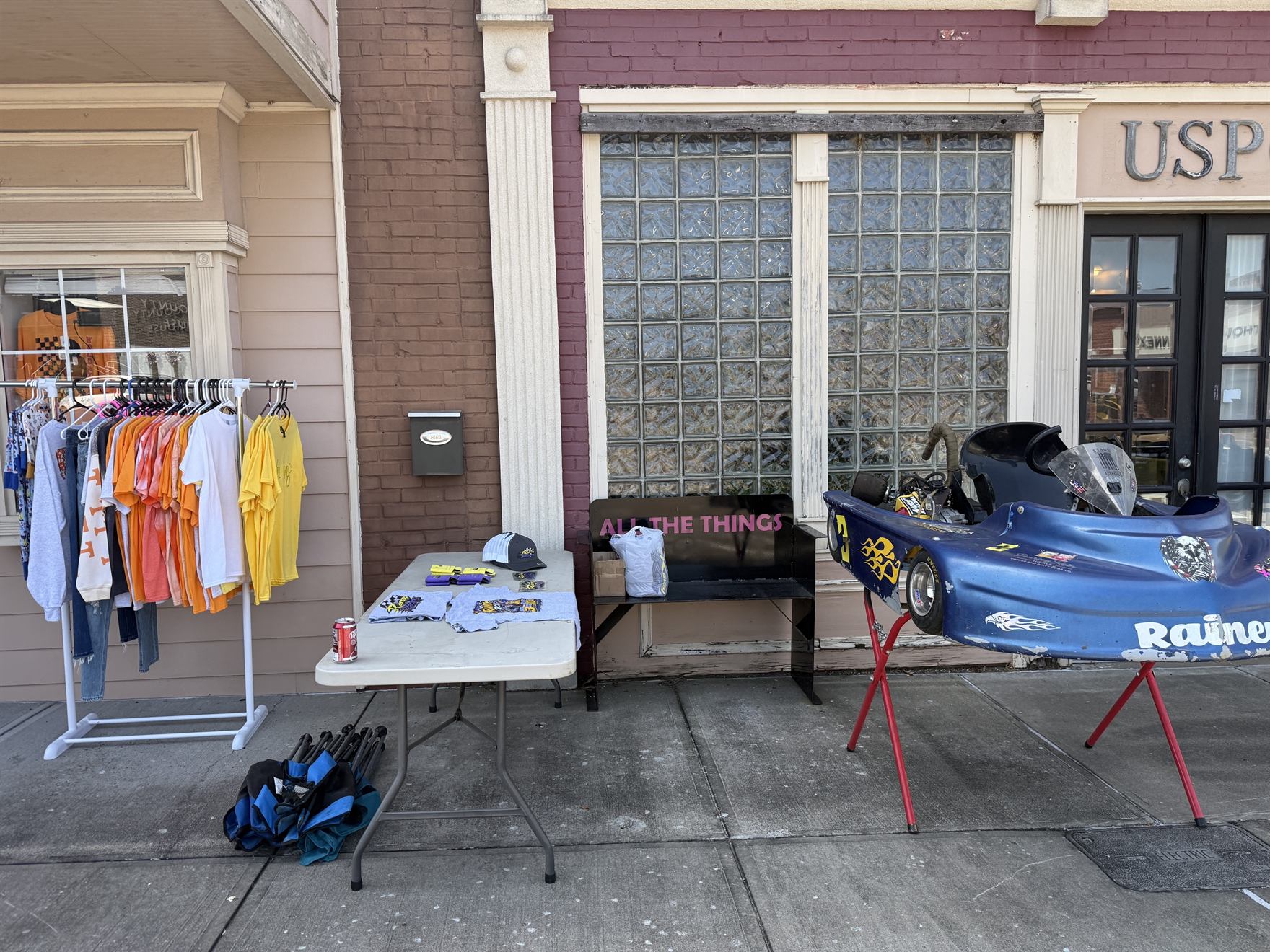 Rainey Racing shirts, hats and koozies laid out on the merch table beside the blue 3 kart