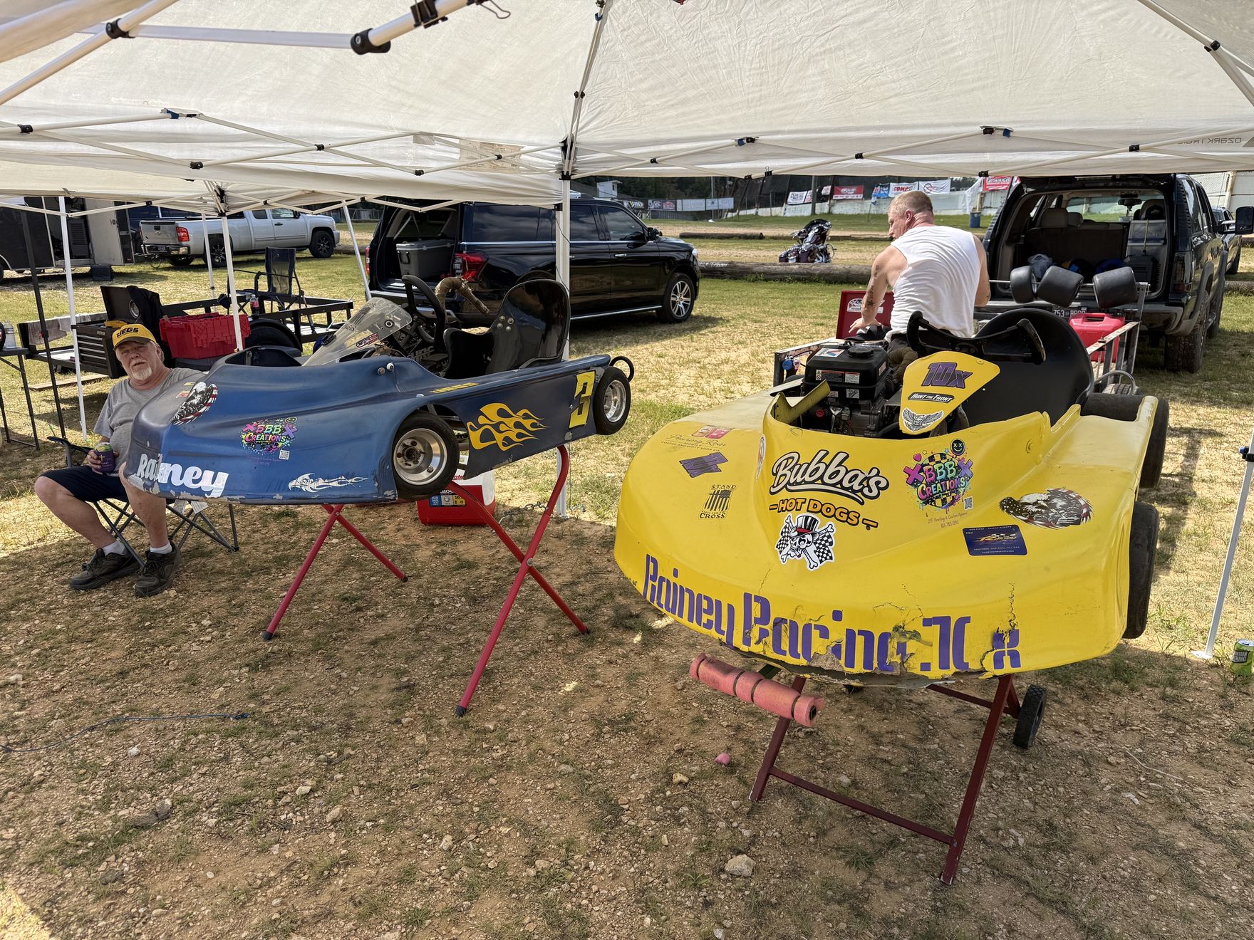 Both Rainey Racing karts under the team canopy in the pits at Camden Speedway, with Ronnie Rainey Sr. sitting alongside