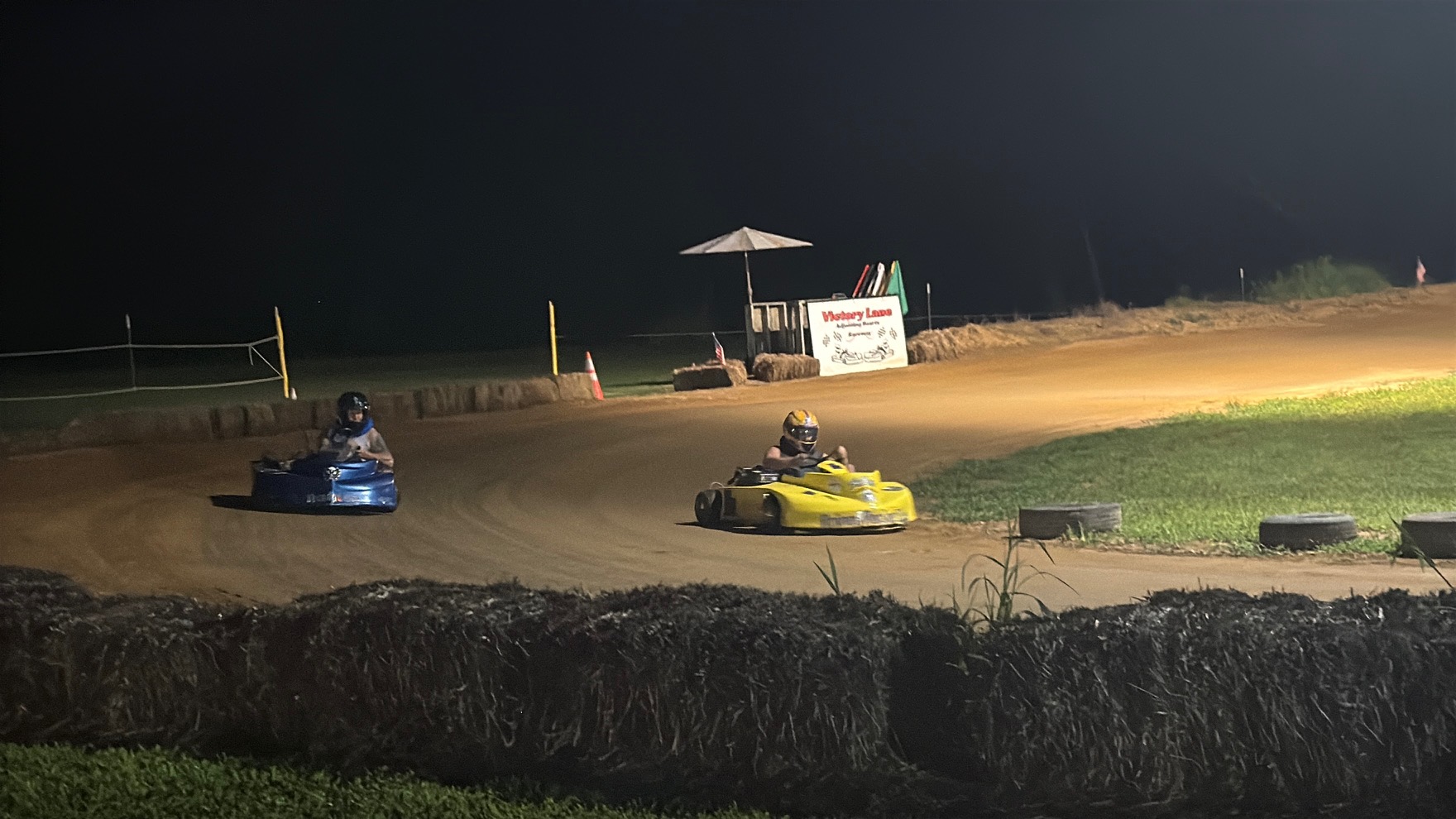 The 10X and the 3 racing side by side under the lights at Adjoining Hearts Raceway, with the Victory Lane sign in the background