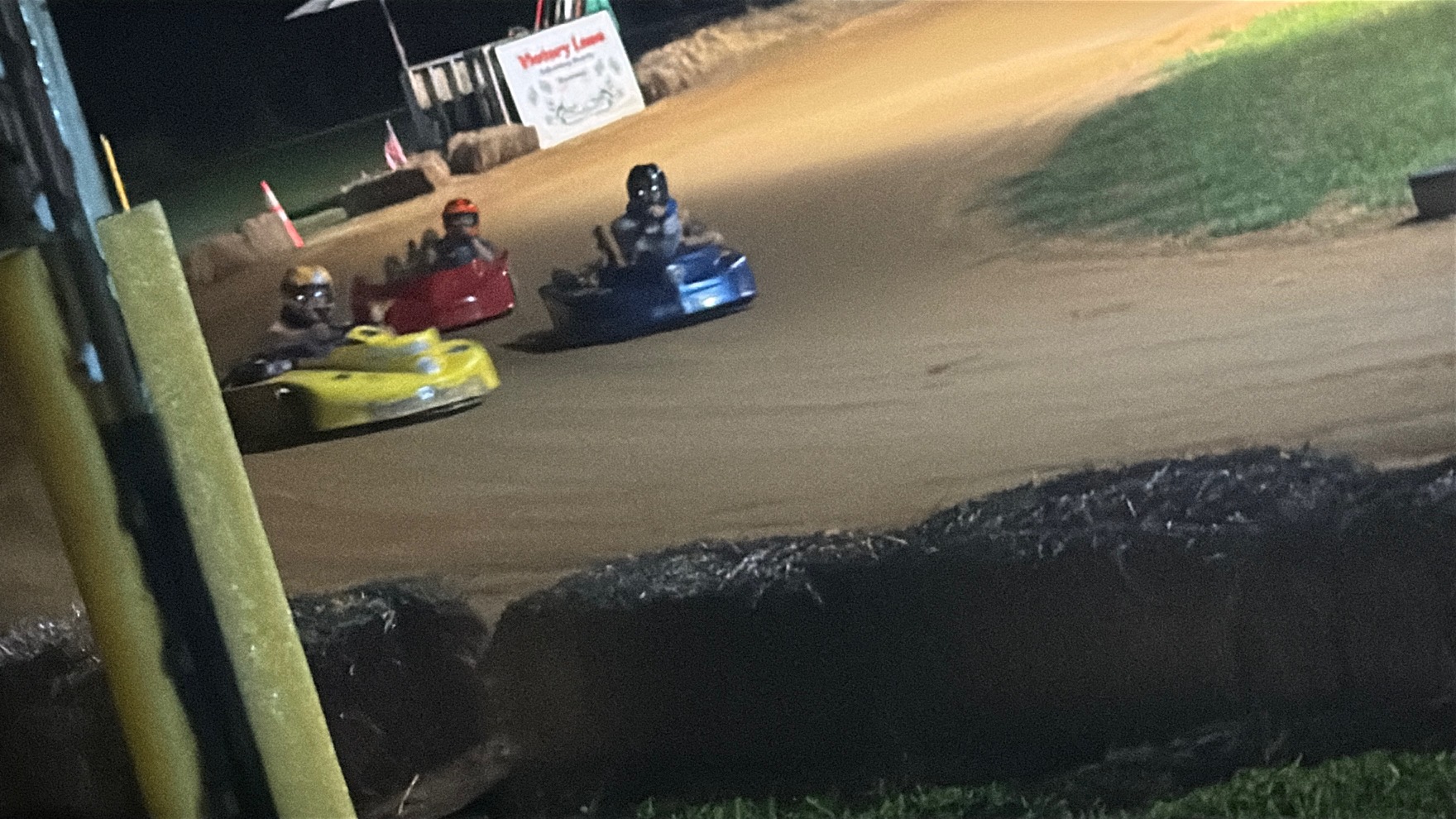 Three karts racing into a corner at night at Adjoining Hearts Raceway