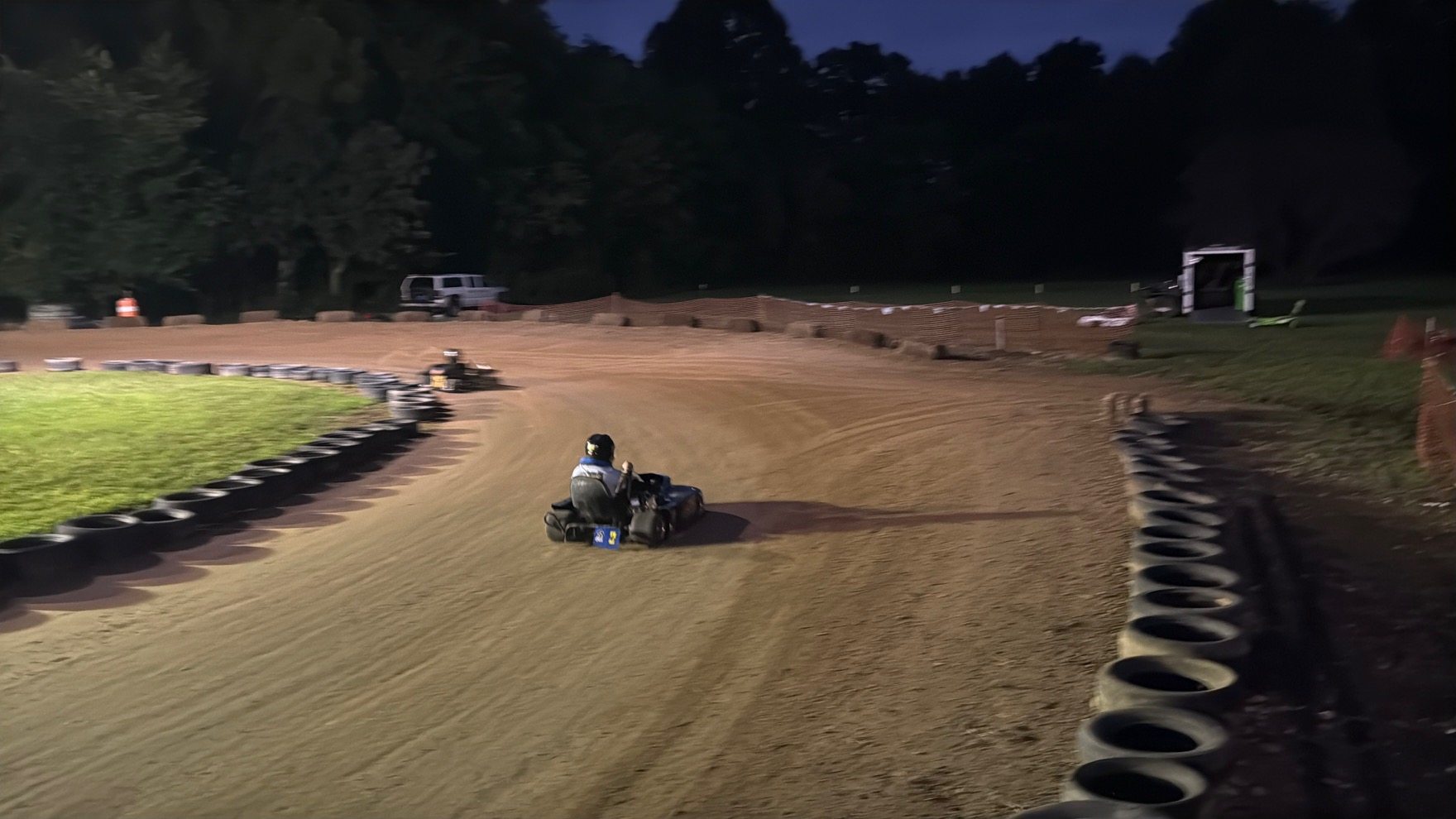 The blue 3 kart running down the back stretch at Sleepy Hollow at twilight, chasing another kart
