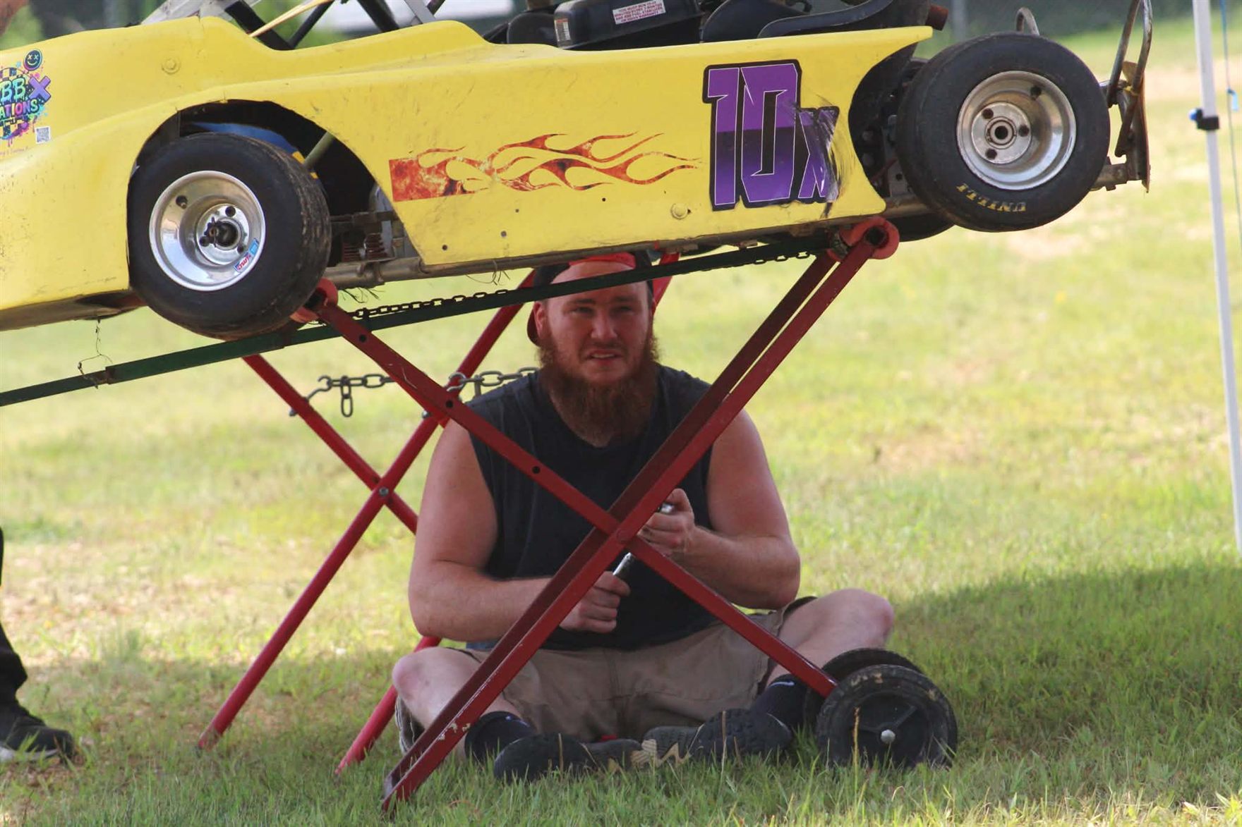A crew member sitting under the 10X kart up on its stand, working between races