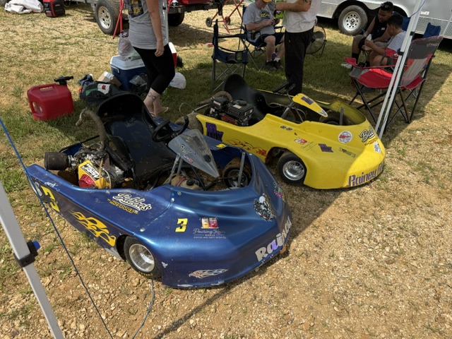 Both Rainey Racing karts in the pits with families and haulers in the background on race day